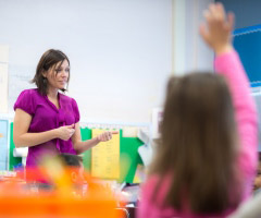 A student raises their hand while a teacher speaks to them
